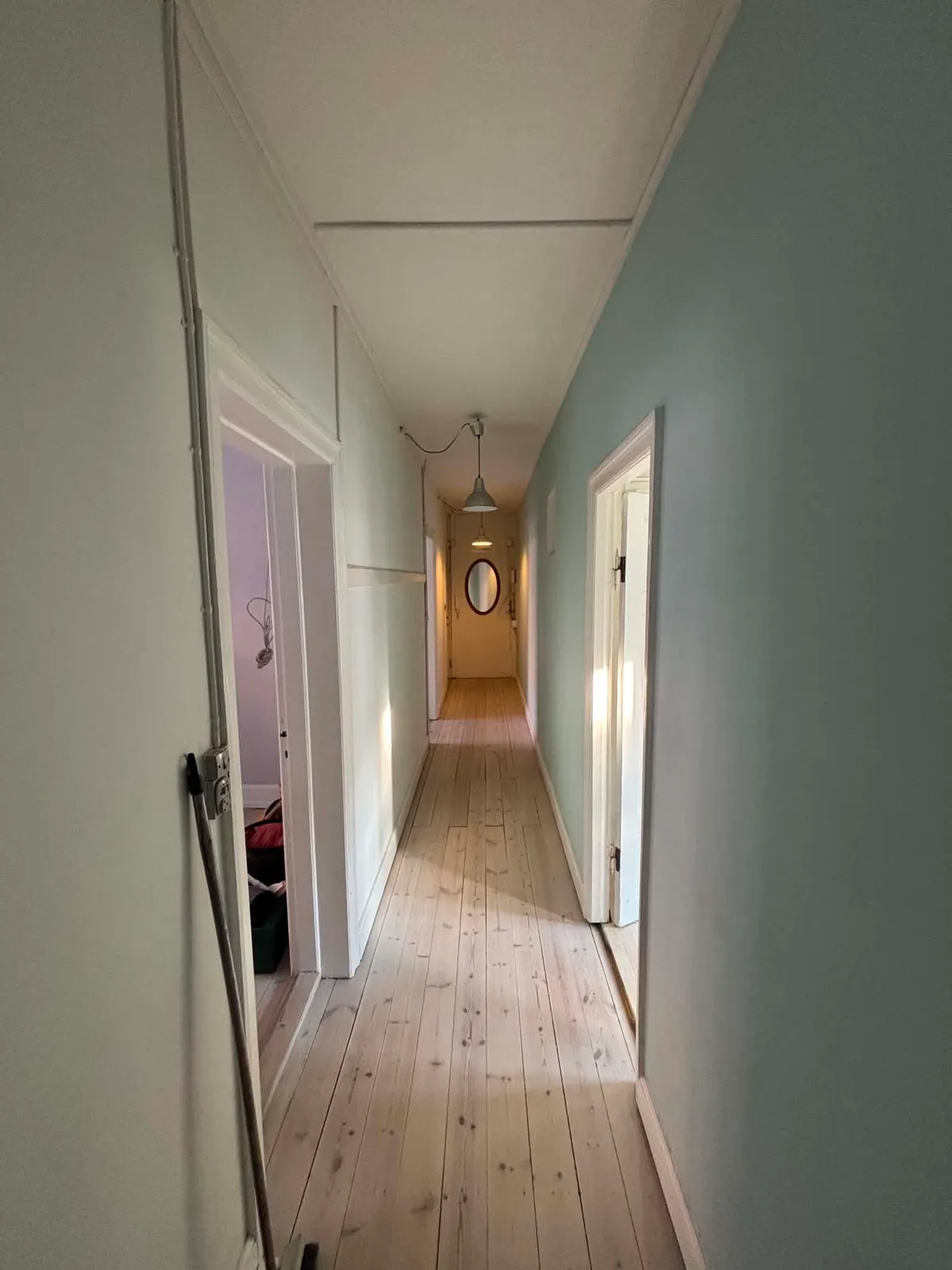 Lang gang med lyst plankegulv og en lysegrøn væg i lejligheden på Amager